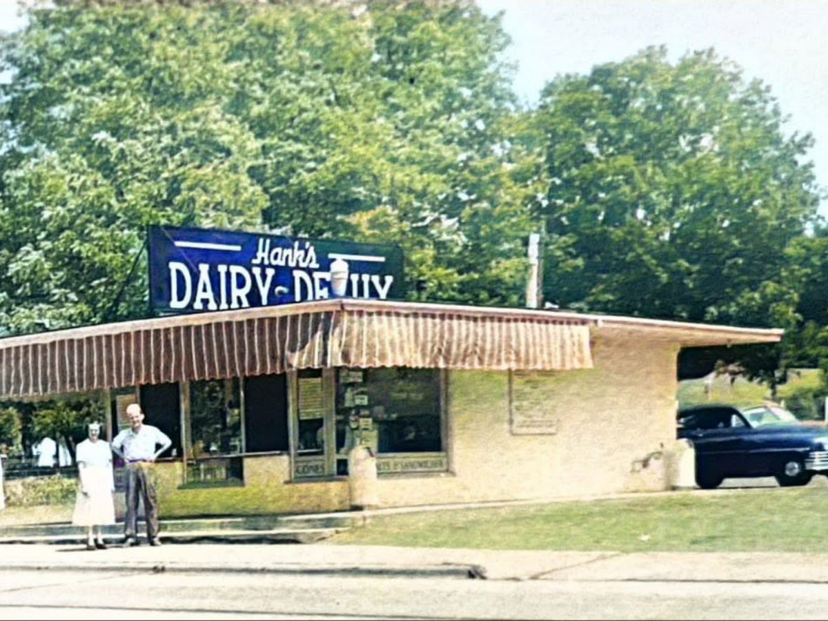 Color photo of Hank's Dairy-Delite stand with two people out front and a 1950s car